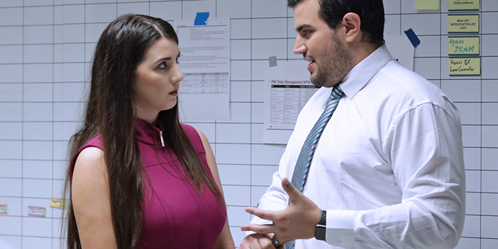 A man and a woman stand in front of whiteboards in an office and engage in conversation.