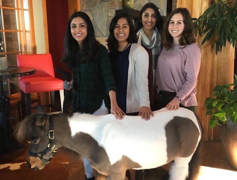 Anisha Panth stands with three other women while petting a small pony.