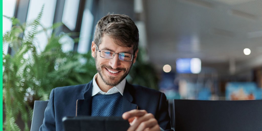 A man in business casual smiles at his device.