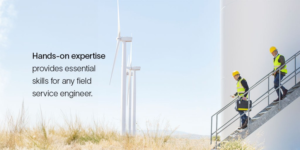 Two field service engineers walk down stairs near a wind mill, demonstrating the value of hands-on experience.