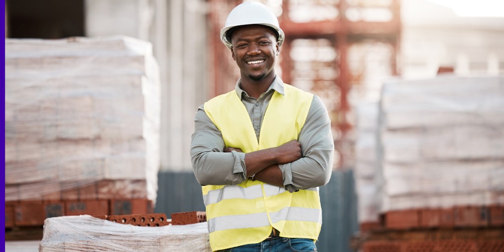 An engineer in a reflective safety vest and hard-hat smiles at the camera