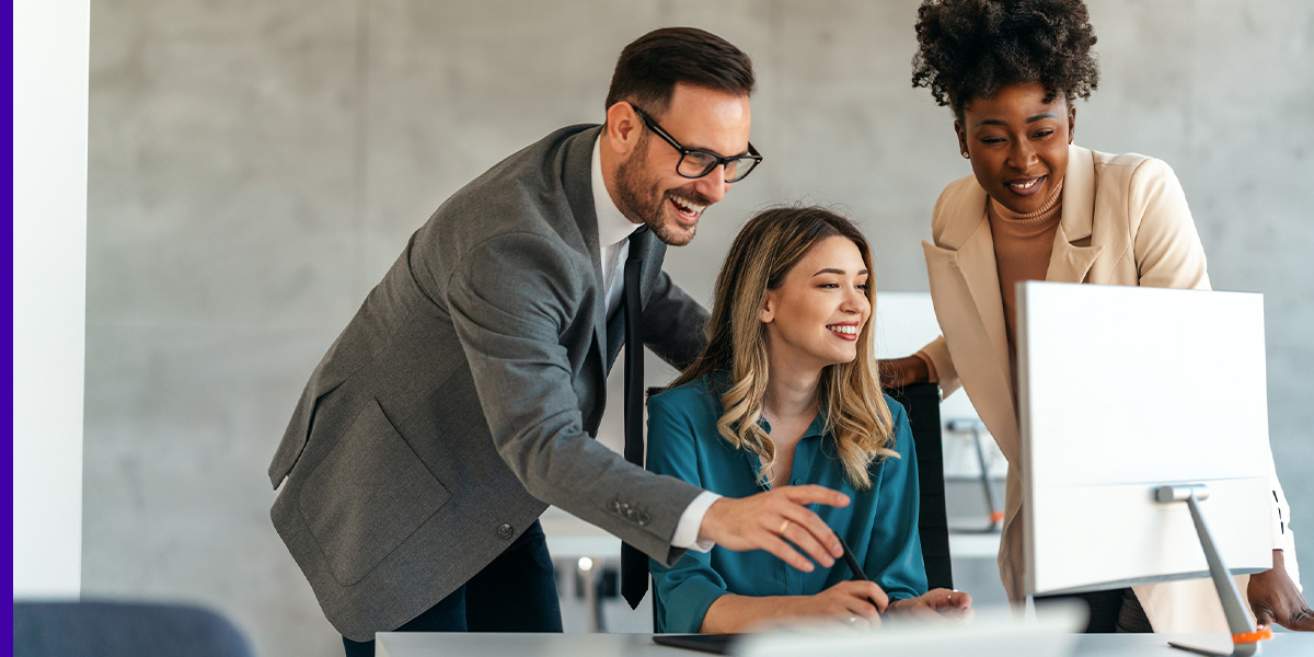 Three professionals look at a computer in an office