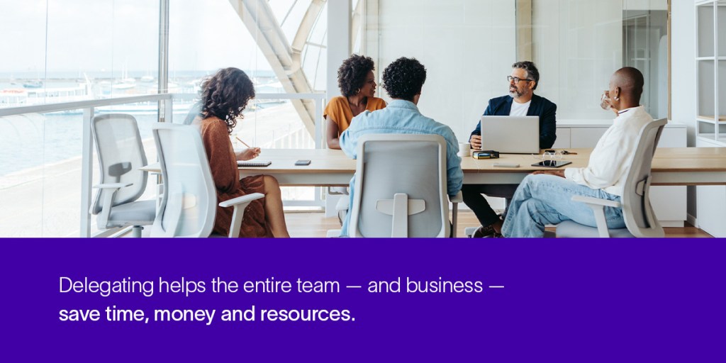 Five professionals sit in a bright office at a table during a team meeting