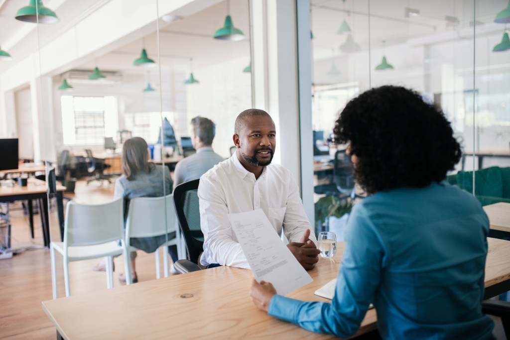 African American man smiling while answering questions during an interview with a manager in a modern office