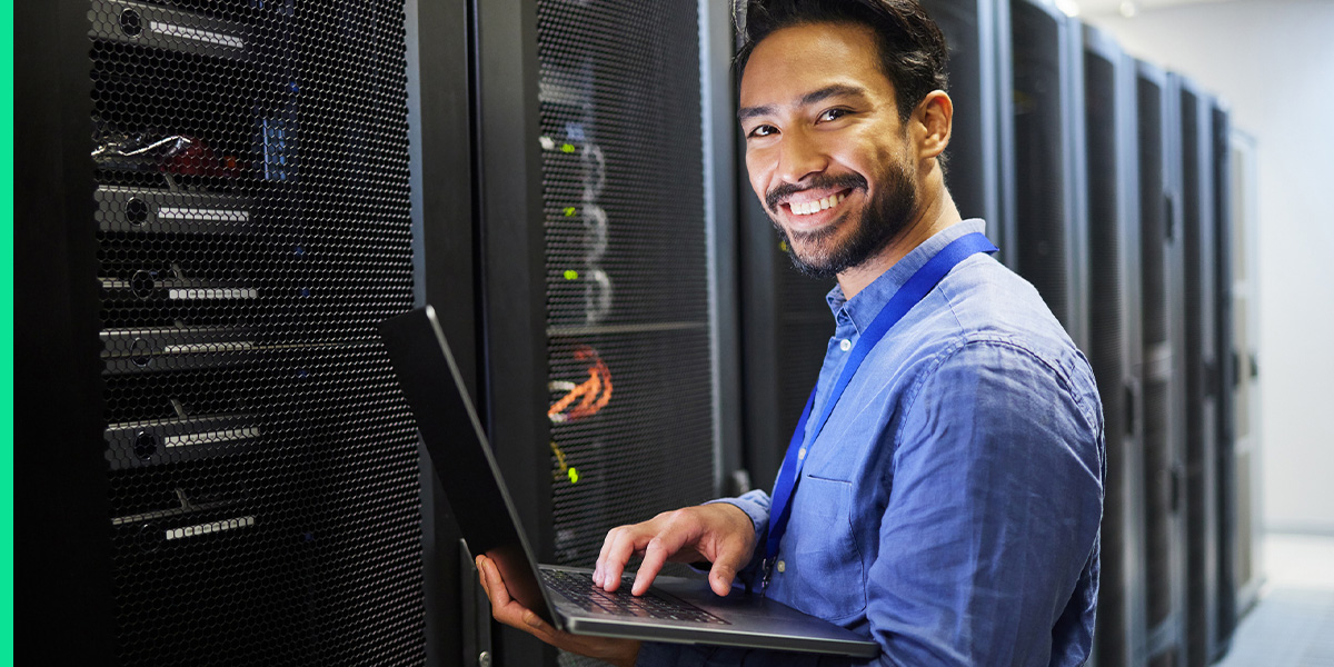 An IT worker holds a laptop in a larger data center