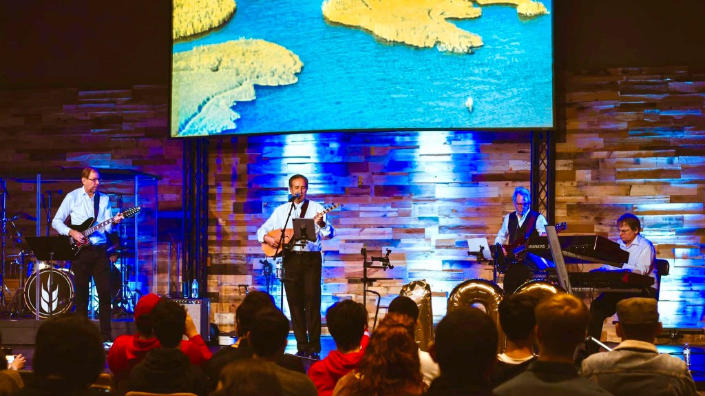 Four men playing instruments in front of a small crowd.