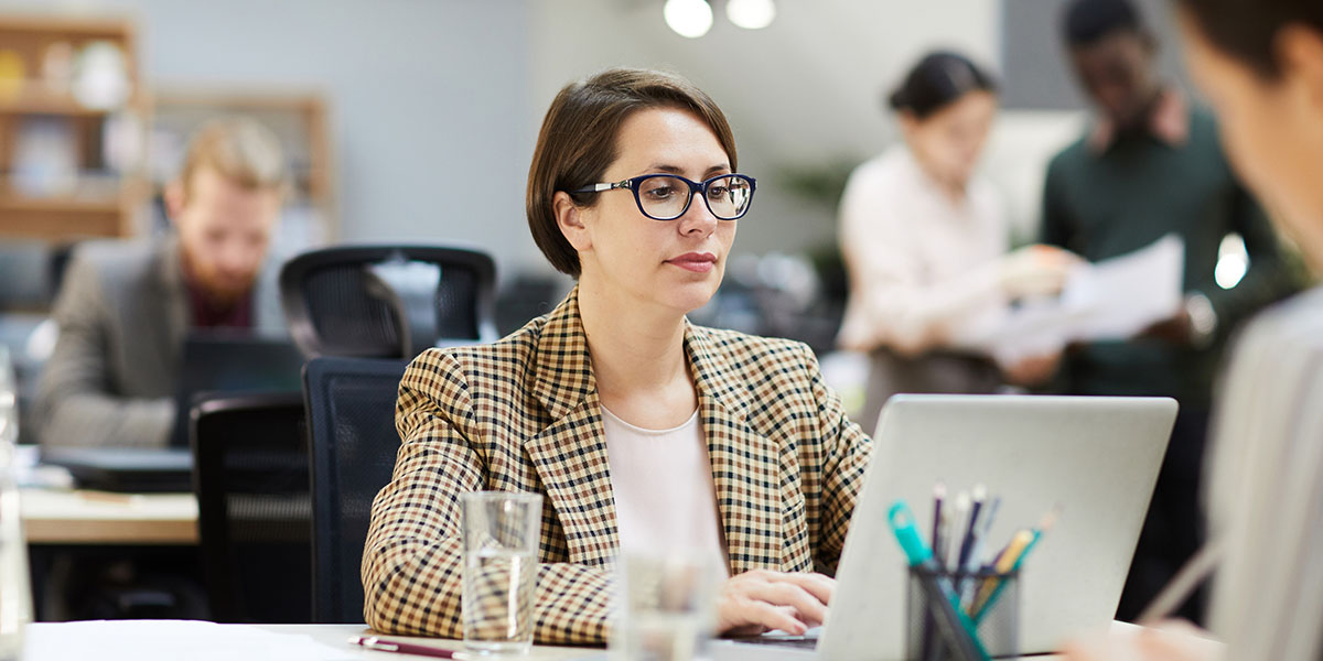 A young professional in a checkered blazer types on a laptop