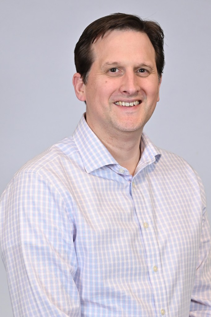 headshot of a man in a white checked shirt on a light gray background