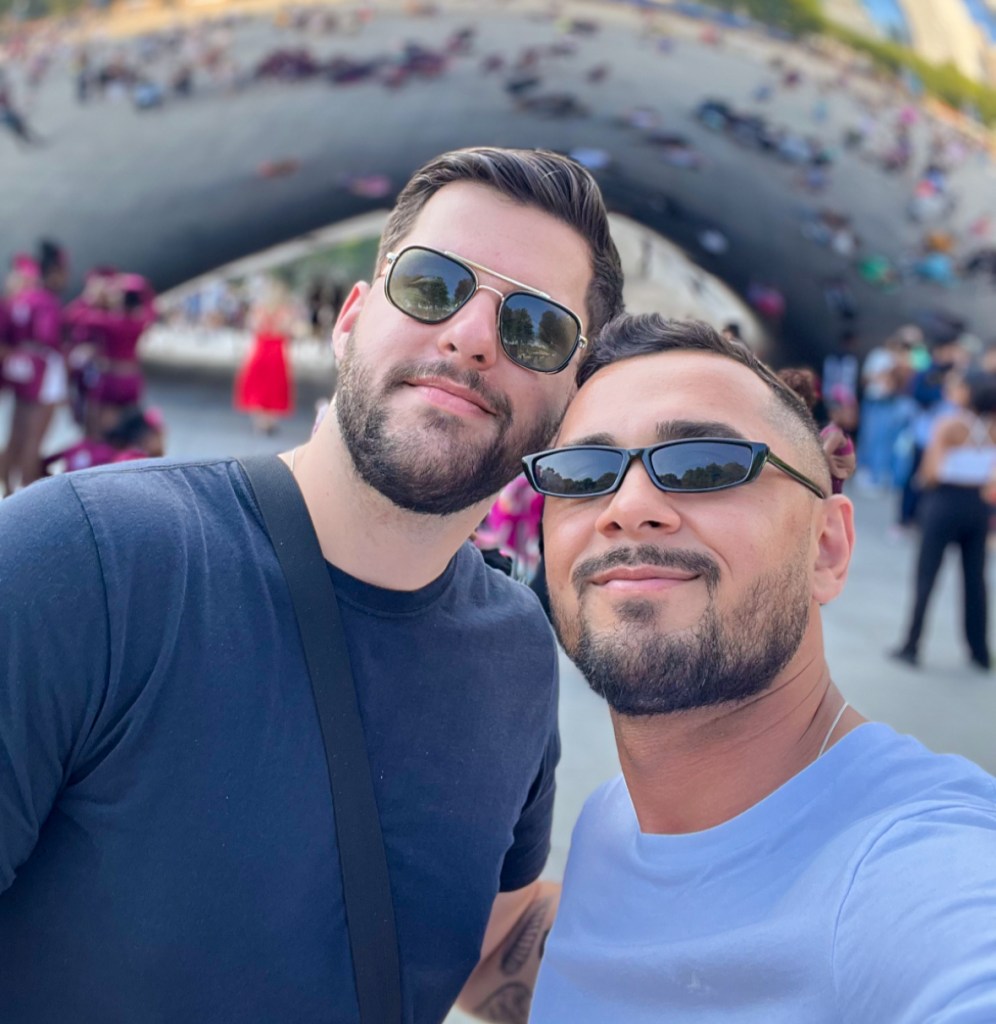 Two men in sunglasses stand in front of Cloud Gate in Chicago