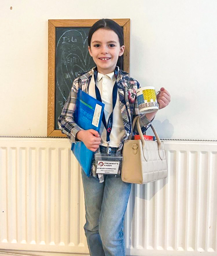 a young girl dressed in a blazer, holding a coffee cup, purse and folder and wearing a Phenomenex branded badge