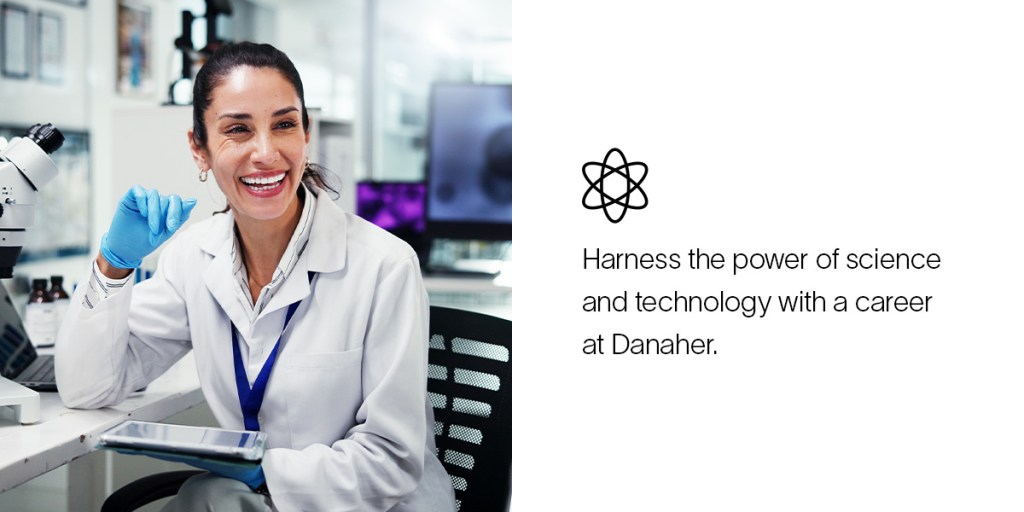 A woman in a lab coat and gloves laughs with colleagues